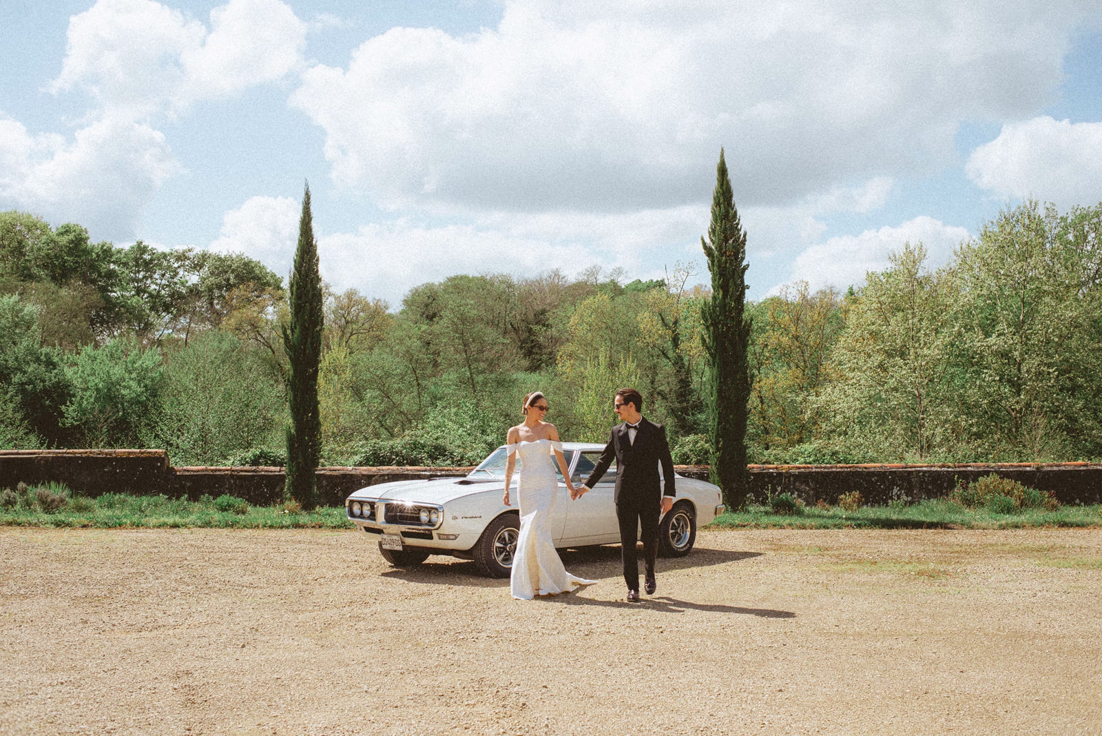 Mariés main dans la main près d’une voiture vintage, série L’Amour Fou IV au Château de Campet